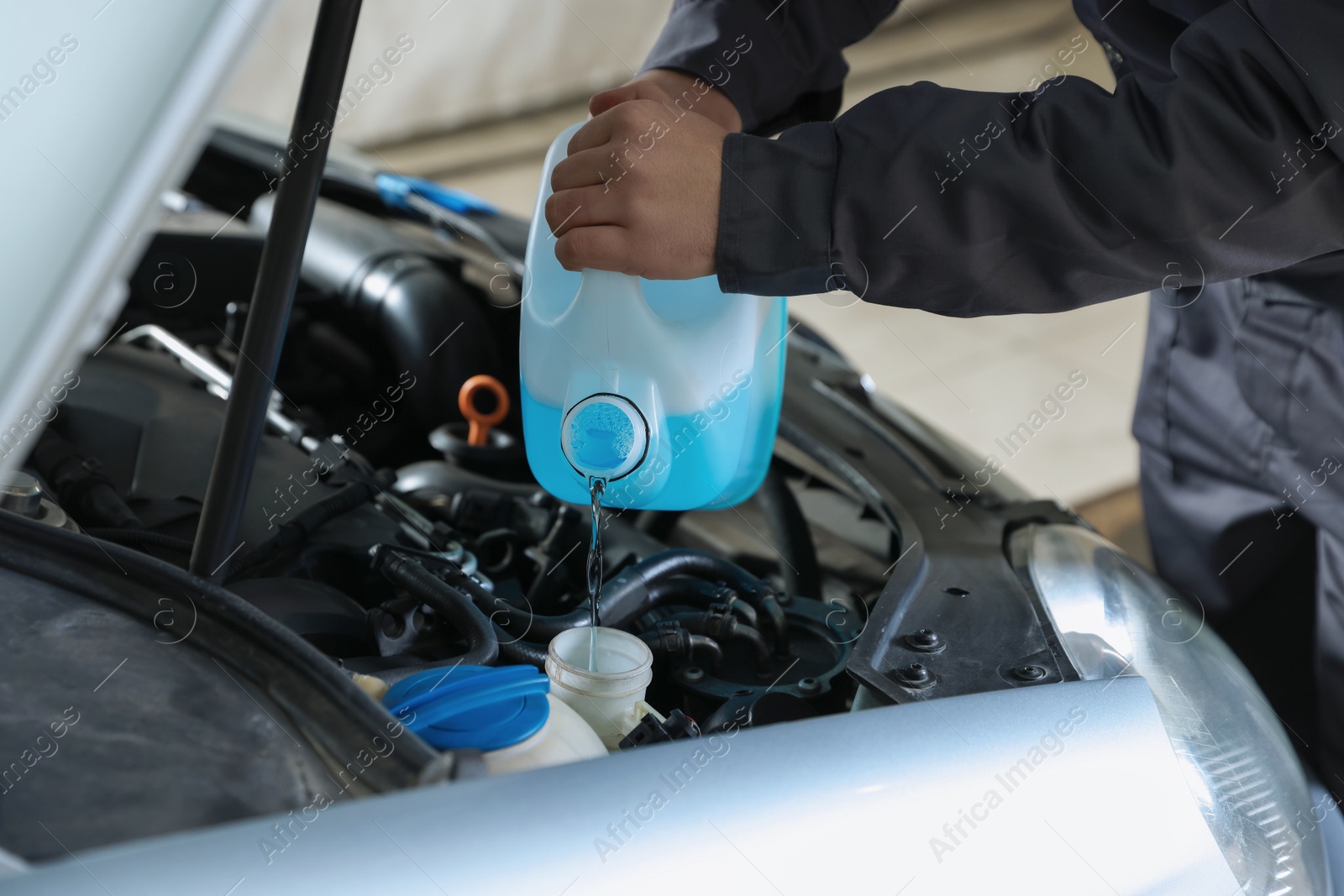 Photo of Man pouring windshield washer from plastic canister into car reservoir outdoors, closeup