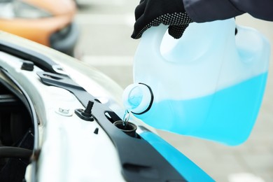 Photo of Man filling car radiator with antifreeze outdoors, closeup