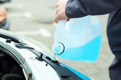 Photo of Man filling car radiator with antifreeze outdoors, closeup