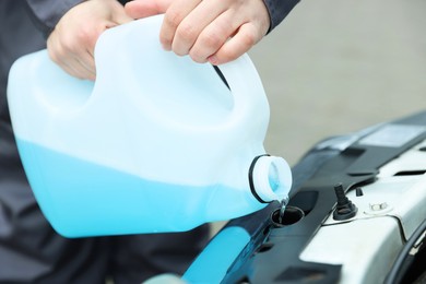 Photo of Man filling car radiator with antifreeze outdoors, closeup