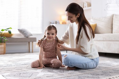 Happy mother with her cute little daughter on carpet at home