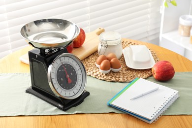 Photo of Retro mechanical kitchen scale, products and stationery on wooden table indoors