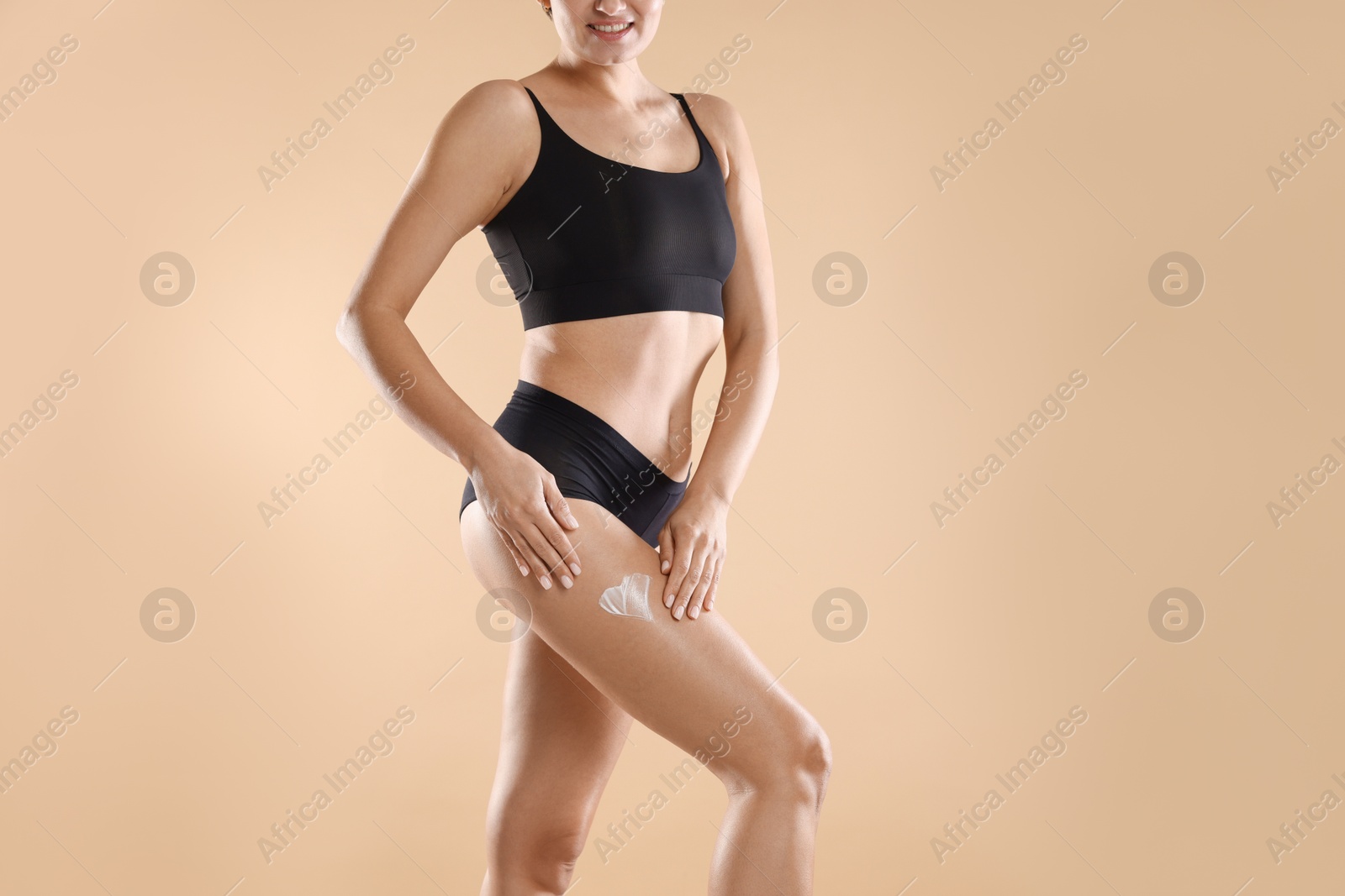 Photo of Woman applying anti cellulite cream on beige background, closeup