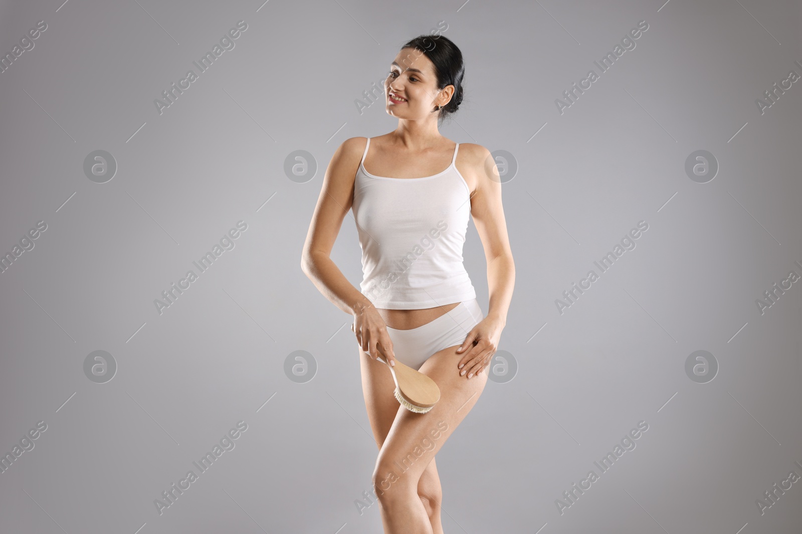 Photo of Woman doing anti cellulite massage with brush on grey background