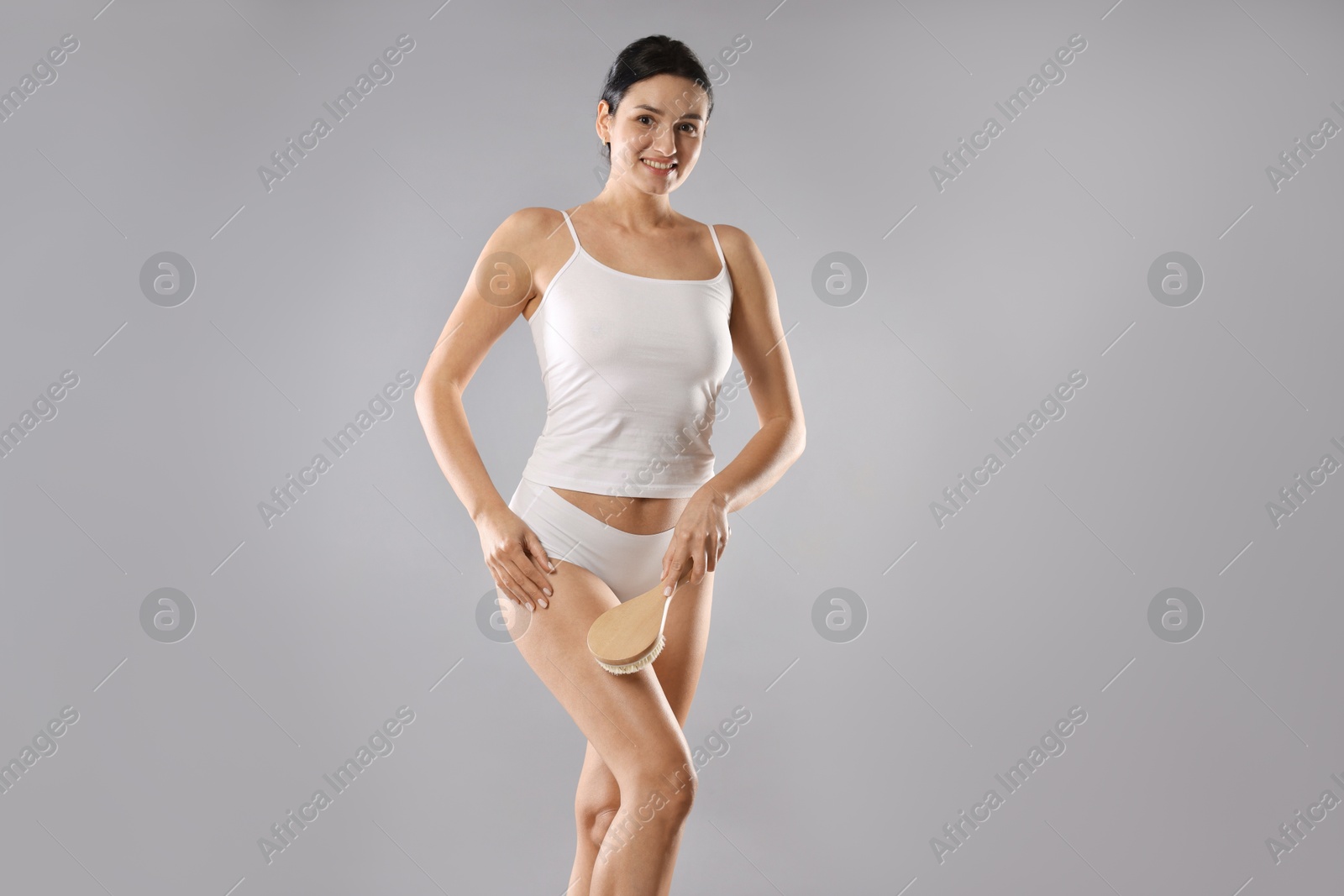 Photo of Woman doing anti cellulite massage with brush on grey background