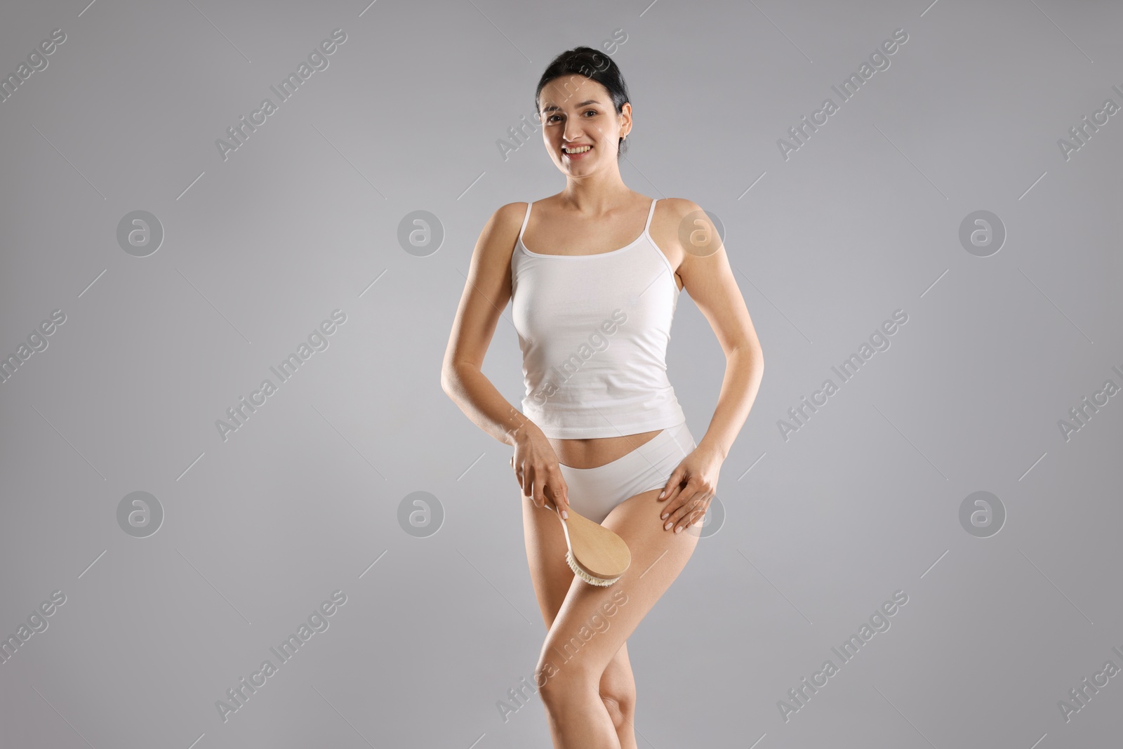 Photo of Woman doing anti cellulite massage with brush on grey background