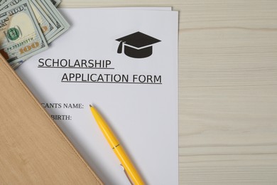 Photo of Scholarship application form, dollar banknotes and pen on wooden table, flat lay. Space for text