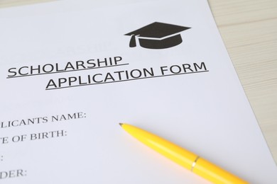 Photo of Scholarship application form and pen on wooden table, closeup