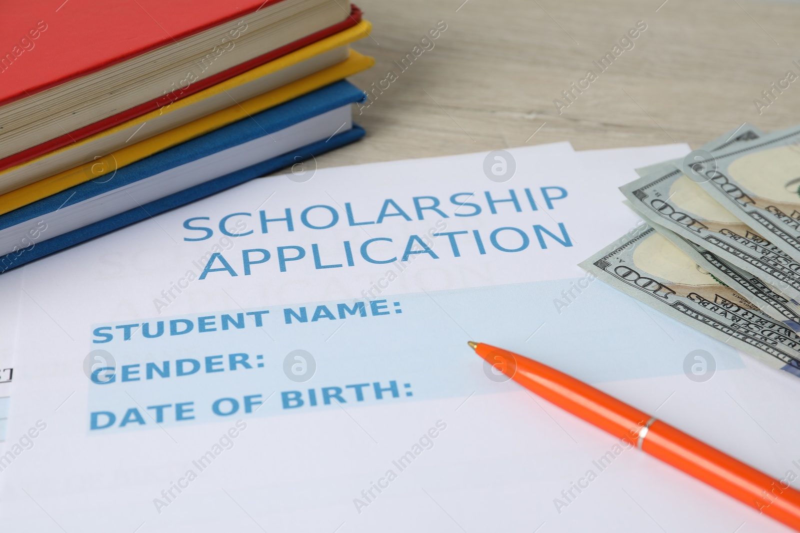 Photo of Scholarship application form, pen, books and dollar banknotes on wooden table, closeup