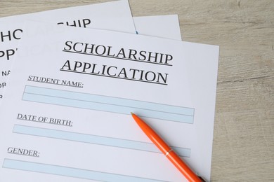 Photo of Scholarship application forms and pen on wooden table, above view