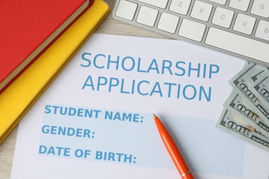 Photo of Scholarship application form, pen, dollar banknotes, computer keyboard and books on wooden table, flat lay