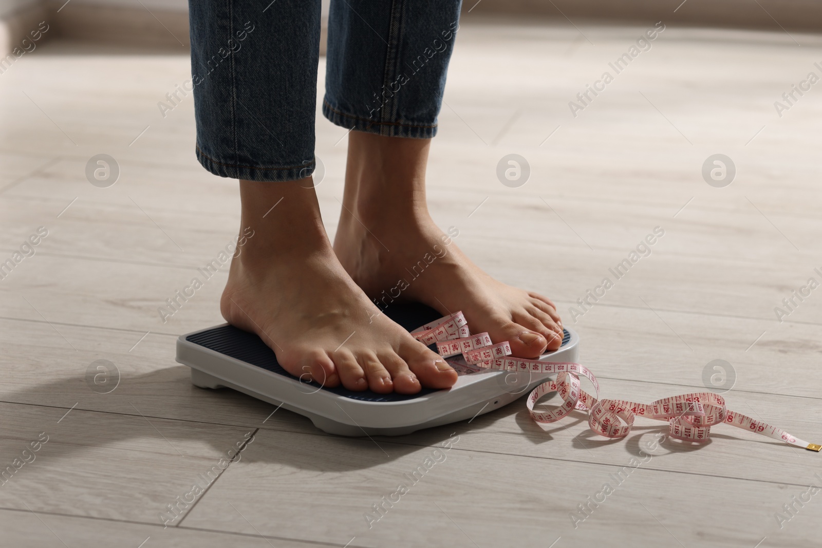 Photo of Woman on scales and measuring tape indoors, closeup. Bulimia problem