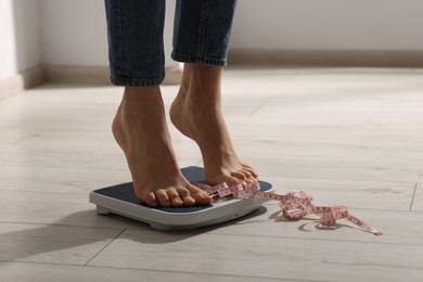 Photo of Woman on scales and measuring tape indoors, closeup. Bulimia problem