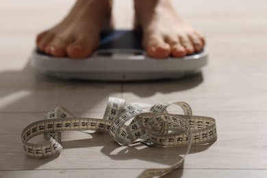 Photo of Woman on scales indoors, focus on measuring tape. Bulimia problem