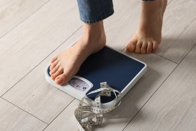 Photo of Woman on scales and measuring tape indoors, closeup. Bulimia problem