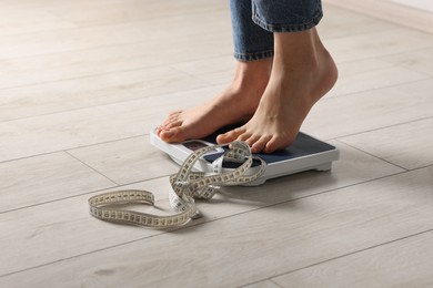 Photo of Woman on scales and measuring tape indoors, closeup. Bulimia problem