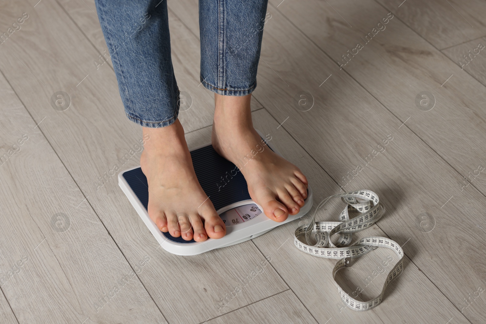 Photo of Woman on scales and measuring tape indoors, closeup. Bulimia problem