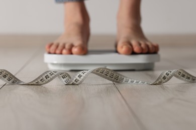 Photo of Woman on scales indoors, focus on measuring tape. Bulimia problem