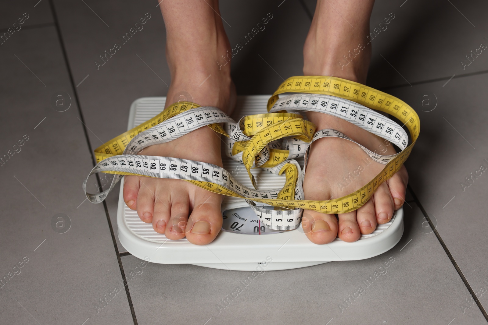 Photo of Woman on scales and measuring tape indoors, closeup. Bulimia problem