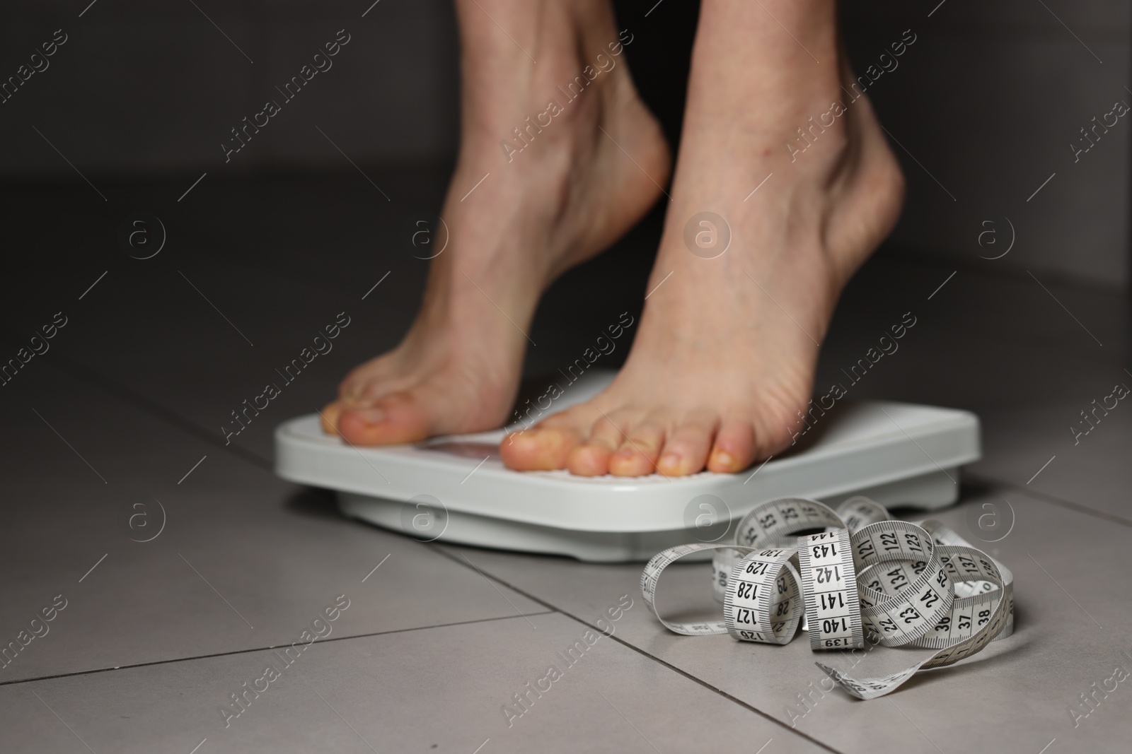 Photo of Woman on scales and measuring tape indoors, closeup. Bulimia problem