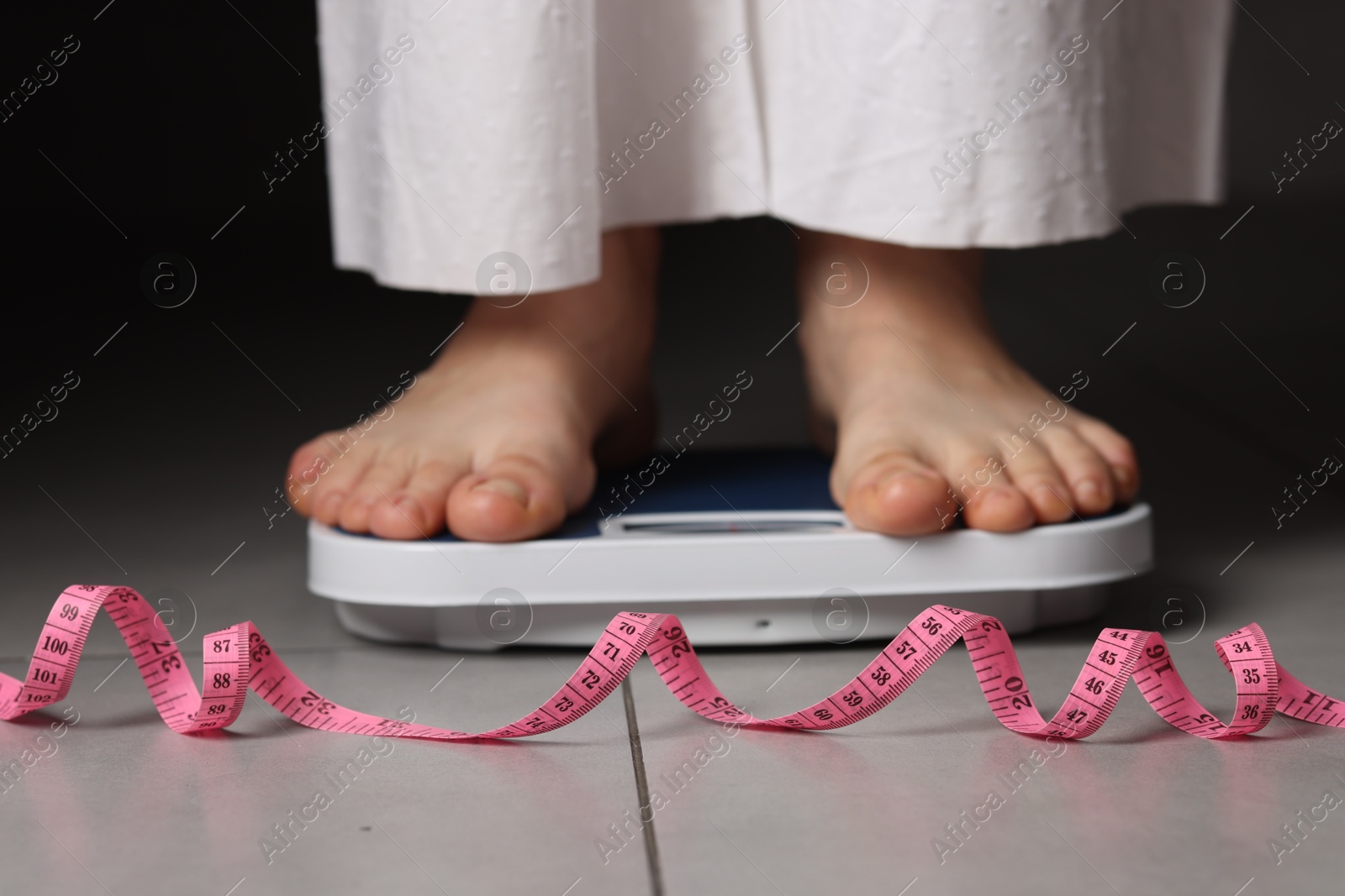 Photo of Woman on scales and measuring tape indoors, closeup. Bulimia problem