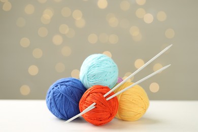 Photo of Balls of colorful yarn and knitting needles on white table against grey background with blurred lights, bokeh effect