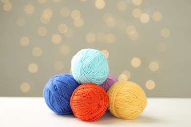 Photo of Balls of colorful yarn on white table against grey background with blurred lights, bokeh effect