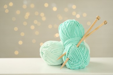 Photo of Skeins of colorful yarn and knitting needles on white table against grey background with blurred lights, space for text. Bokeh effect