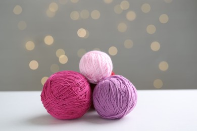 Balls of colorful yarn on white table against grey background with blurred lights, bokeh effect