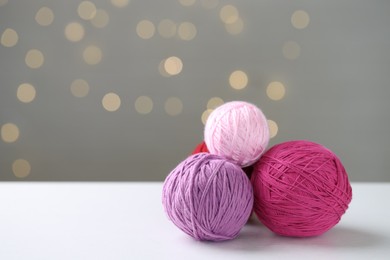 Balls of colorful yarn on white table against grey background with blurred lights, space for text. Bokeh effect