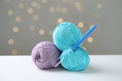 Colorful yarns and crochet hook on white table against grey background with blurred lights, bokeh effect