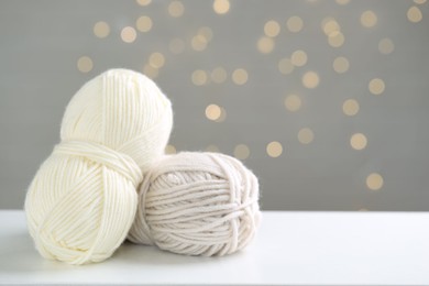 Skeins of yarn and knitting needles on white table against grey background with blurred lights, space for text. Bokeh effect