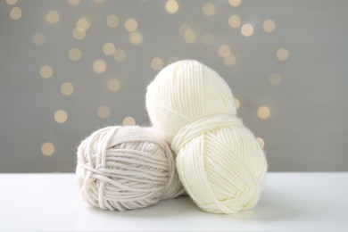 Skeins of yarn and knitting needles on white table against grey background with blurred lights, bokeh effect