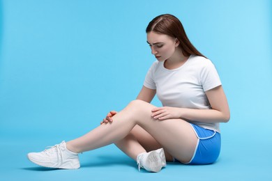 Photo of Young woman suffering from pain in knee on light blue background. Space for text