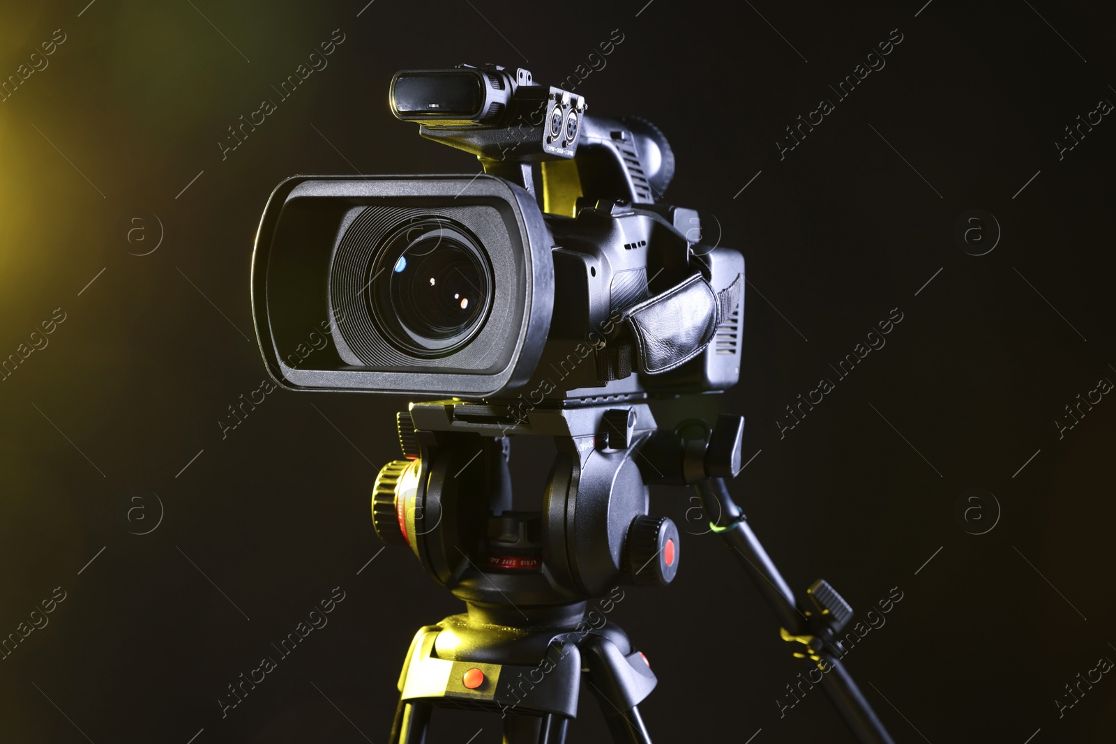 Photo of Modern video camera with tripod on black background, closeup