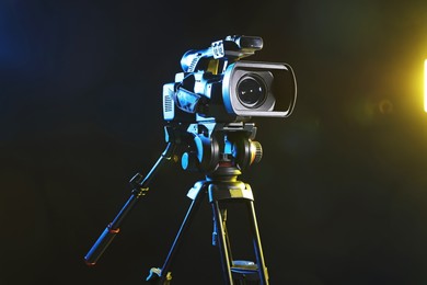 Photo of Modern video camera with tripod on black background