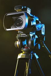 Modern video camera with tripod on black background, closeup