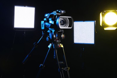 Photo of Modern video camera with tripod and lighting equipment on black background