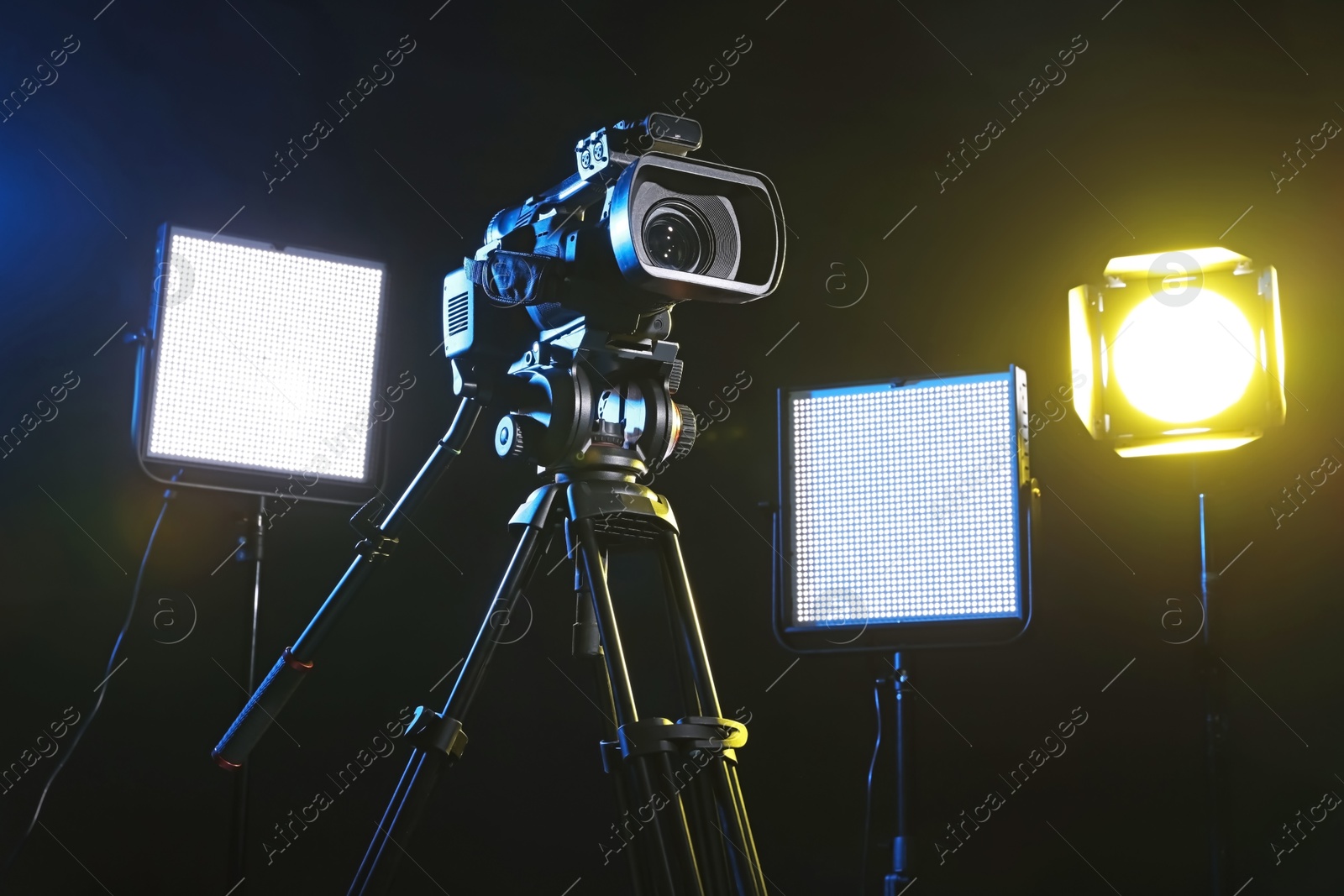 Photo of Modern video camera with tripod and lighting equipment on black background