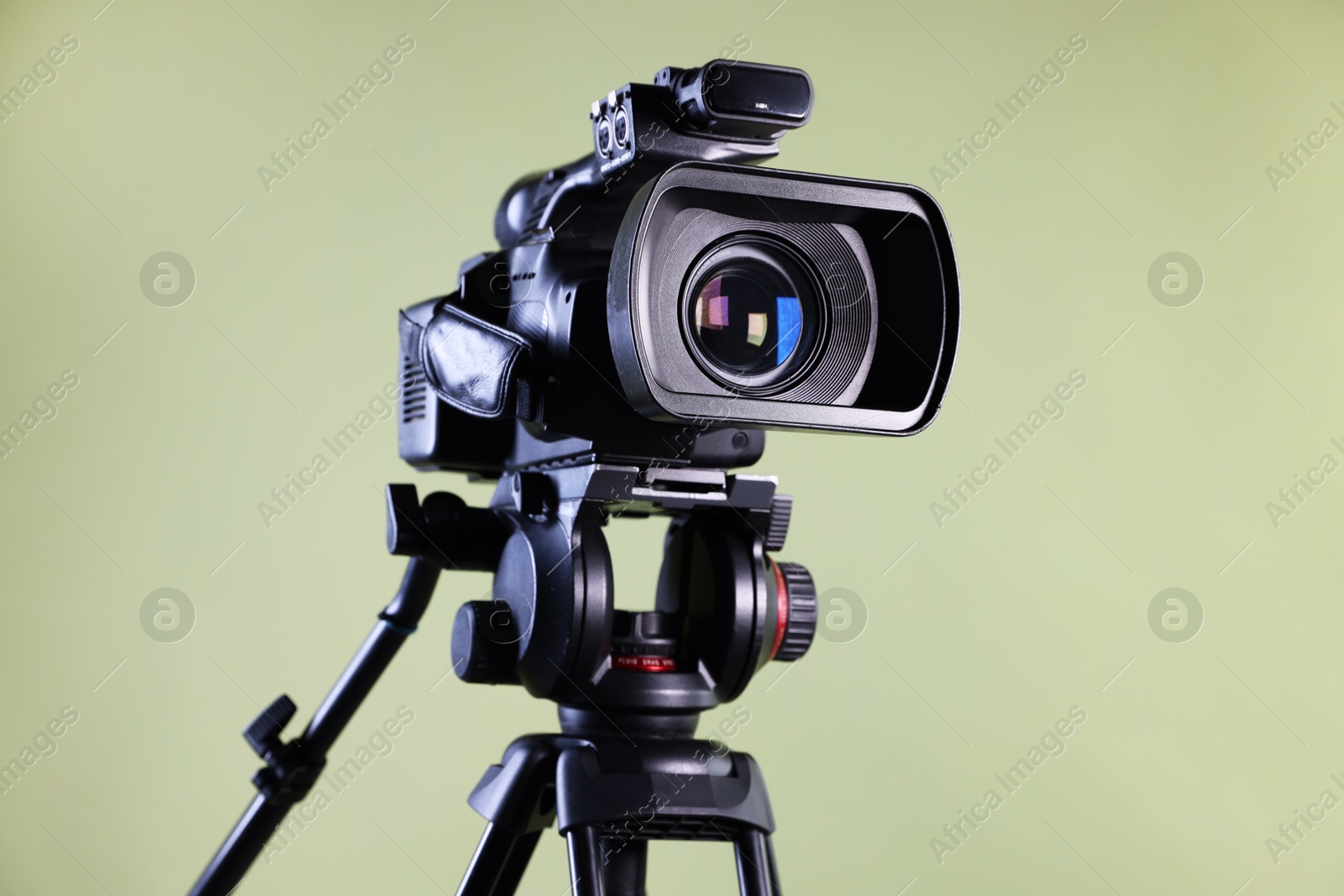 Photo of Modern video camera with tripod on light olive background