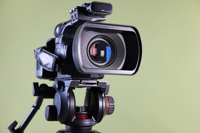 Photo of Modern video camera on light olive background, closeup