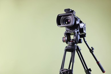 Photo of Modern video camera with tripod on light olive background, space for text