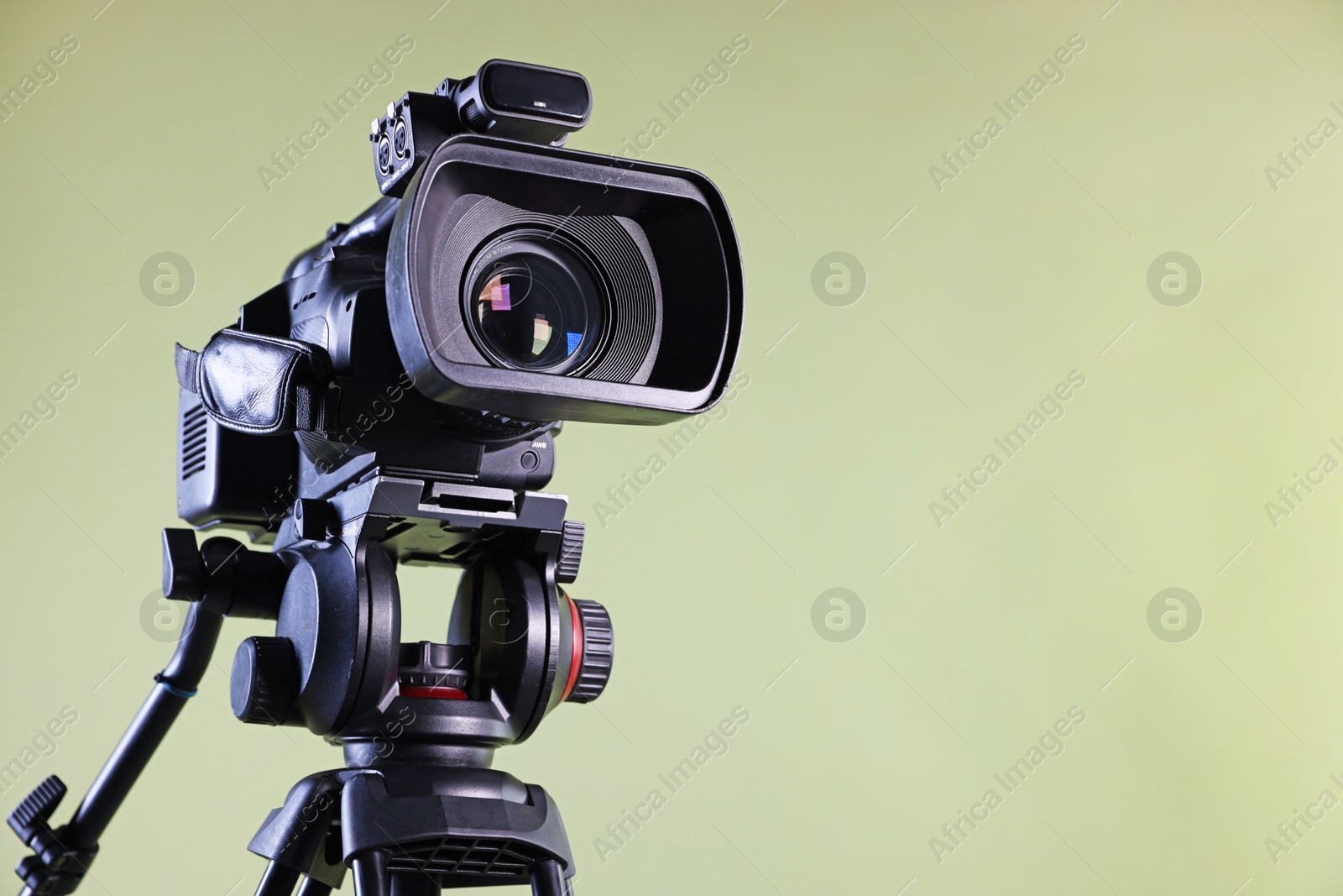 Photo of Modern video camera on light olive background, closeup. Space for text