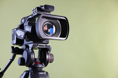 Photo of Modern video camera on light olive background, closeup. Space for text