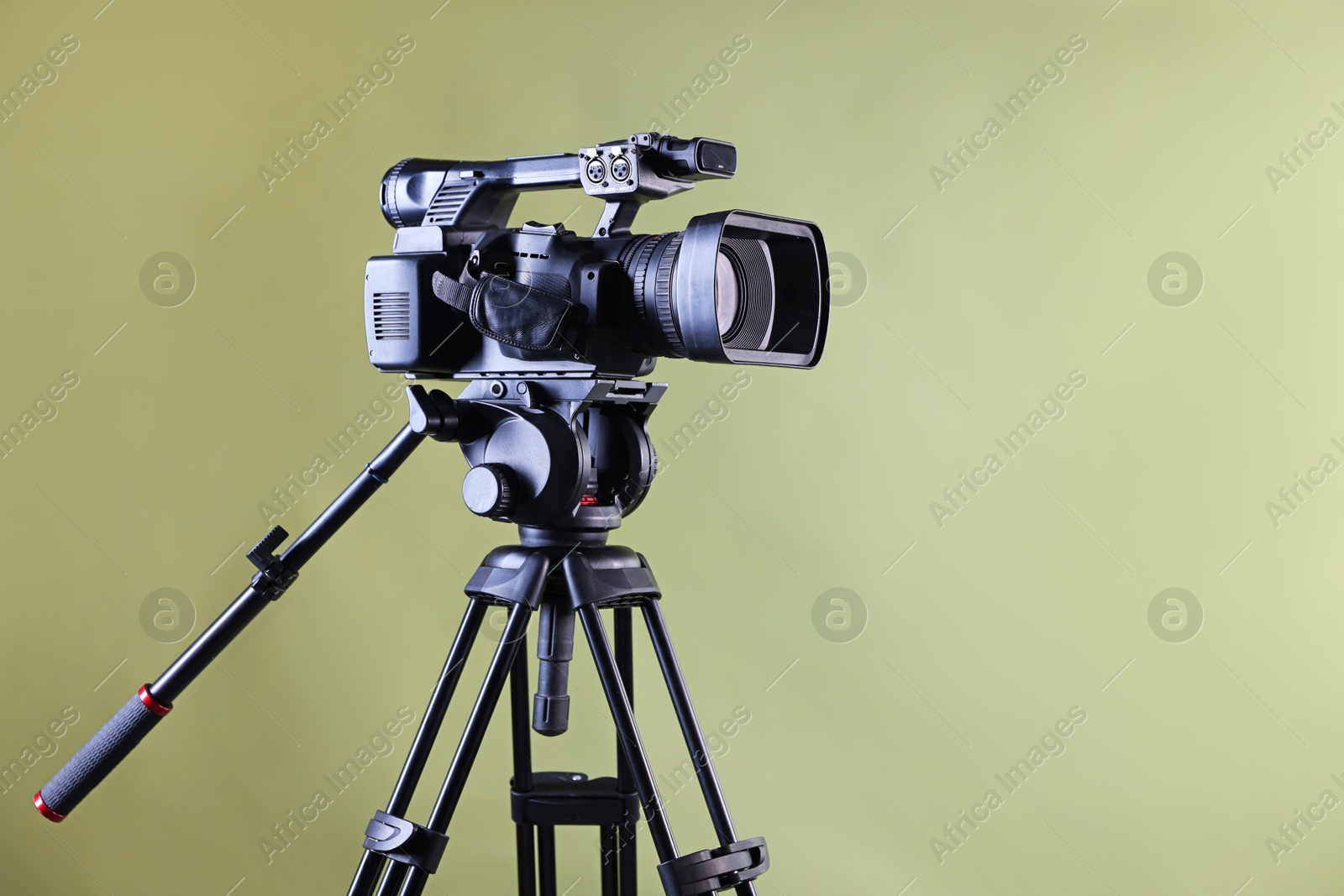 Photo of Modern video camera with tripod on light olive background, space for text