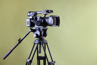 Modern video camera with tripod on light olive background, space for text