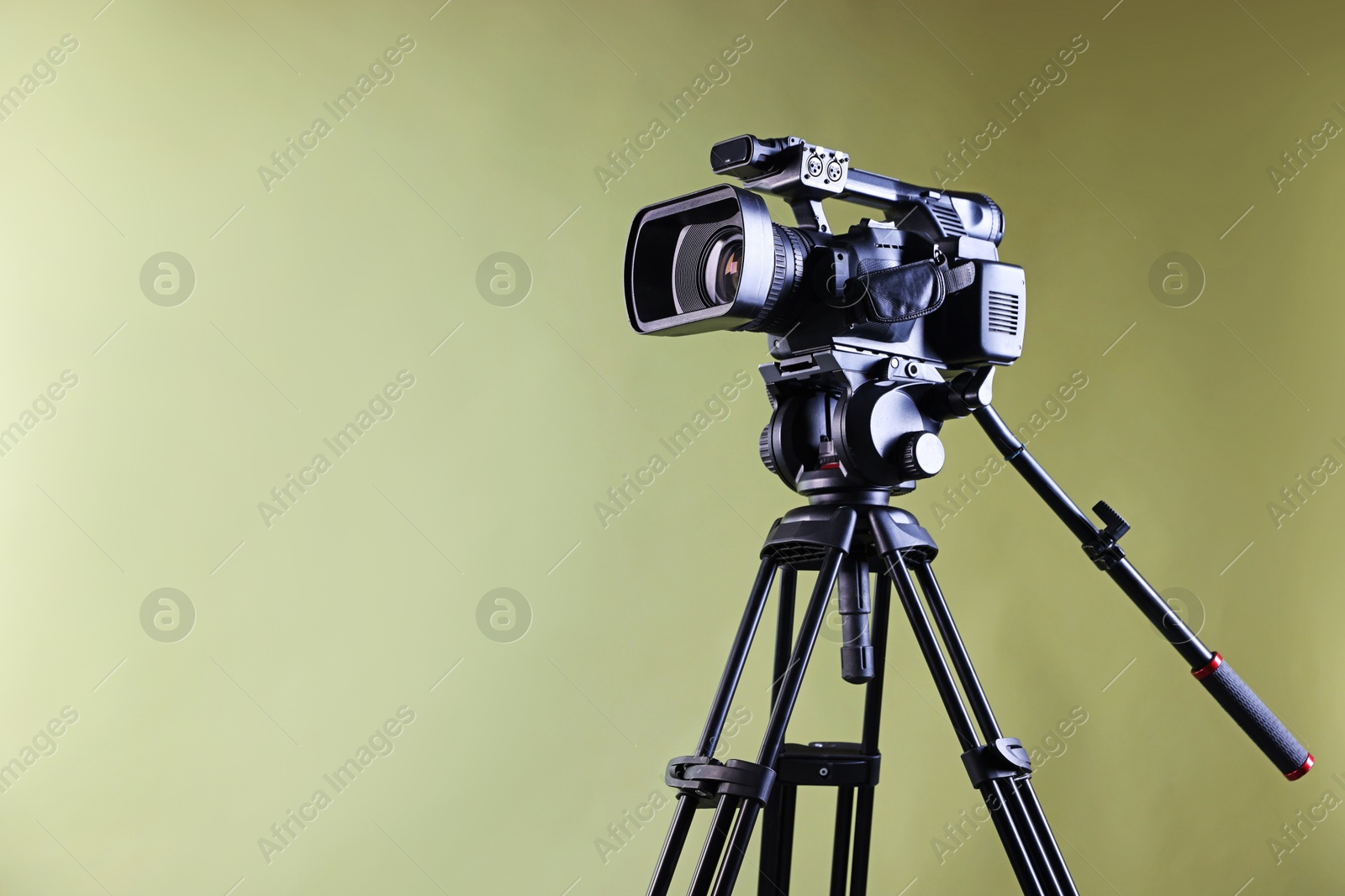 Photo of Modern video camera with tripod on light olive background, space for text