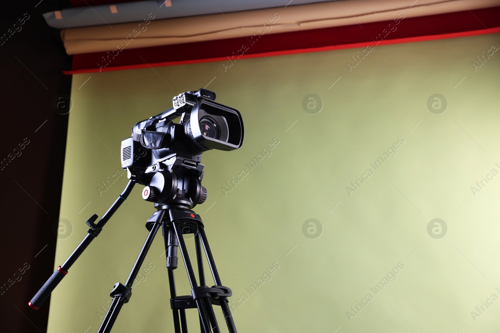 Photo of Modern video camera with tripod in studio, low angle view. Space for text