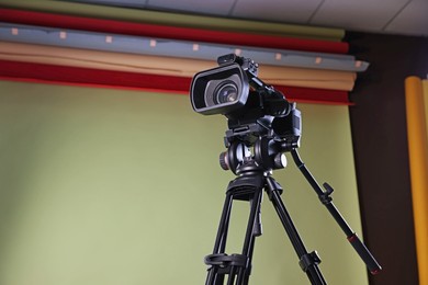 Modern video camera with tripod in studio, low angle view. Space for text