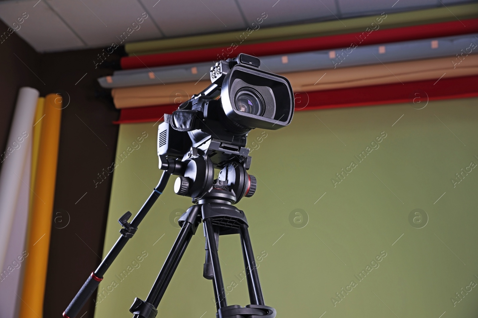 Photo of Modern video camera with tripod in studio, low angle view. Space for text